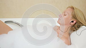 Beautiful woman taking a bath and listening to music on headphones. cell phone