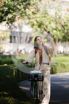 Beautiful woman taking a bike stroll in the park, business woman holding smartphone using bike rental, business woman