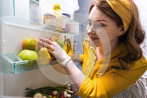 beautiful woman taking fruits from fridge