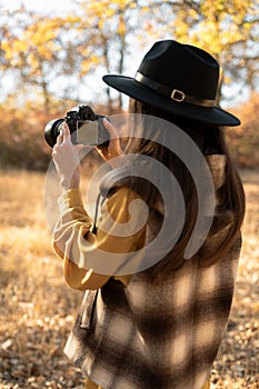 Beautiful woman taking pictures in autumn forest. Rest, tourism and hobby concept.