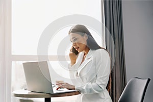 Beautiful woman talking on phone while working on laptop computer.