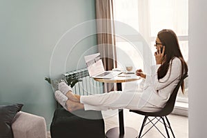 Beautiful woman talking on phone while working on laptop computer