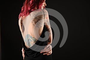 Beautiful woman with tattoos on body against background, back view. Space for text photo