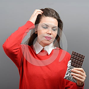 Beautiful woman in temptation of eating a chocolate against gray background