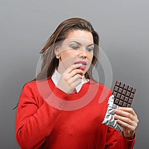 Beautiful woman in temptation of eating a chocolate against gray background