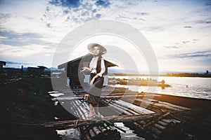 Beautiful woman in Thai local dress standing on boat in fishing village with field and lake background