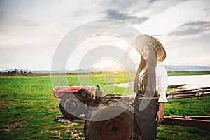 Beautiful woman in Thai local dress standing nearby mini tractor with field and lake background