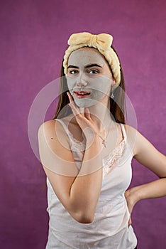 Beautiful woman with therapeutic green clay facial mask  on purple