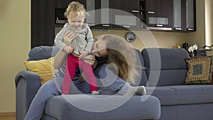 Beautiful woman tickle toddle child stomach sitting on sofa.