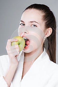 Beautiful woman with tied hair bites an apple showing snow-white teeth. Healthy oral cavity