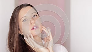 Beautiful woman touching her face, applying organic cosmetic cream with facial massage lines, glowing healthy skin and