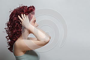 Beautiful woman touching her red curly hair against white background