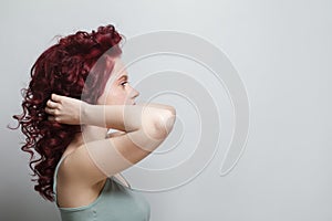 Beautiful woman touching her red curly hair against white studio wall background