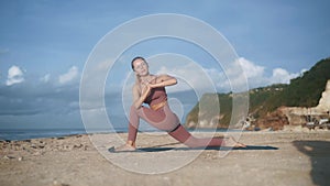 Beautiful woman in tracksuit practises yoga poses on beach