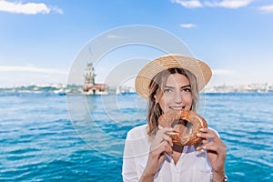 Beautiful woman traveler eats traditional Turkish street food simitbagelin front of Maiden Tower,a popular destination in Istanb