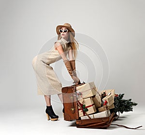 Beautiful woman traveler in hat with big open leather retro bag full of christmas present gifts