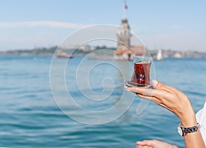 Beautiful woman traveler holds traditional Turkish tea glass in background of Maiden Tower,a popular destination in Istanbul,