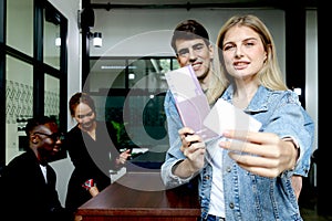 Beautiful woman traveler with long blonde hair shows credit card, holds passport went checking in at hotel reception counter desk