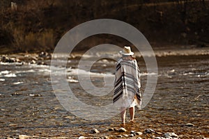 beautiful woman traveler wearing hat and poncho standing in water of river, stylish outfit, boho travel concept, space for text