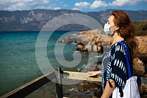 Beautiful woman travels during quarantine in a mask by the sea and beach.