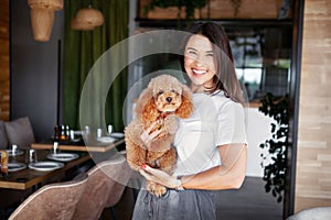 Beautiful woman with two dogs in restaurant. Portrait of female model smiling, looking at camera and holding pets on