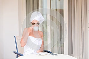 Beautiful woman in under eye patches with cup of coffee and towel on her head. Happy female on vacation enjoying fresh air in