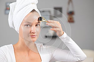 Beautiful woman is using anti aging derma roller. Woman is making needles procedure on face using meso roller photo