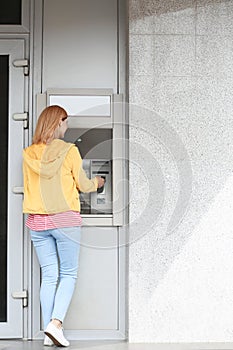 Beautiful woman using cash machine for money withdrawal outdoors