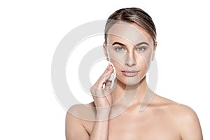 Beautiful woman using cotton pad to remove make up, looking at camera smiling. Beauty and skincare concept.