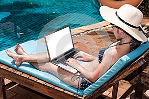 Beautiful Woman using laptop computer luxury relaxing sitting deck chair on resort near swimming pool