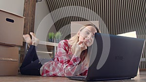 Beautiful woman is using a laptop excited smiling to find new stuff while sitting on the floor near the moving boxes