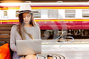 Beautiful woman is using laptop at train station before charming beautiful asian woman travel to destination. She is a blogger and photo