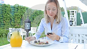 Beautiful woman using smartphone and eating salad in cafe