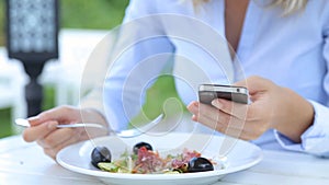 Beautiful woman using smartphone and eating salad in cafe in city