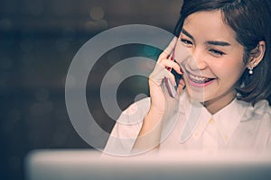 Beautiful woman using smartphone while working with laptop