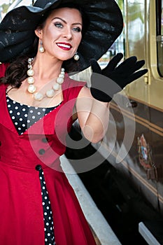 Beautiful woman in vintage red polka dot dress standing on vintage railway platform.