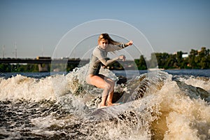 Beautiful woman wakesurfer skilfully riding on splashing wave on a warm day