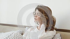 Beautiful woman waking up in bed in morning. Sick woman massaging neck.