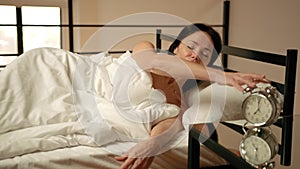 Beautiful Woman Waking Up in Pristine White Bedroom Disabling Alarm