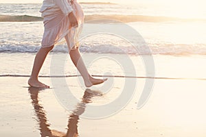 Beautiful woman walk on the beach with sea surf at sunset