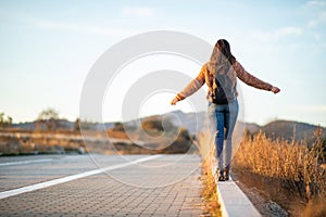 Beautiful woman walking and balancing on street curb or curbstone during sunset