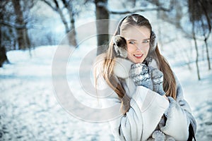 Beautiful woman walking in earmuff, knitted mittens and fur coat have fun in winter forest