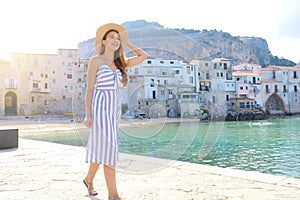 Beautiful woman walking by sea quay in summer day in the seaside town of Cefalu, Italy