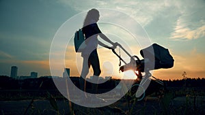 Beautiful woman walking with a stroller in city park at sunset