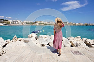 Beautiful woman walking towards Otranto bay admiring panoramic, Apulia, Italy