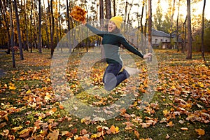 Beautiful woman in warm green pull-over, yellow woolen and casual denim hat jumping high with a bouquet of beautiful dry autumn