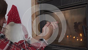 Beautiful woman warming her hands by the fireplace.