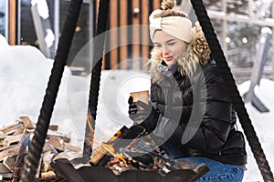 Beautiful woman warming up by the fire pit during cold winter day