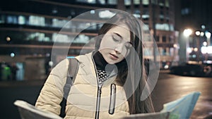 A beautiful woman is watching a close-up map at night in the city.