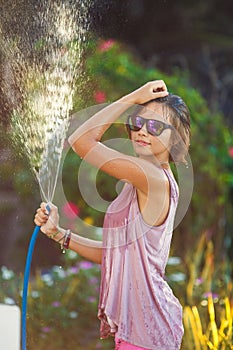 Beautiful woman watering roses with a garden hose